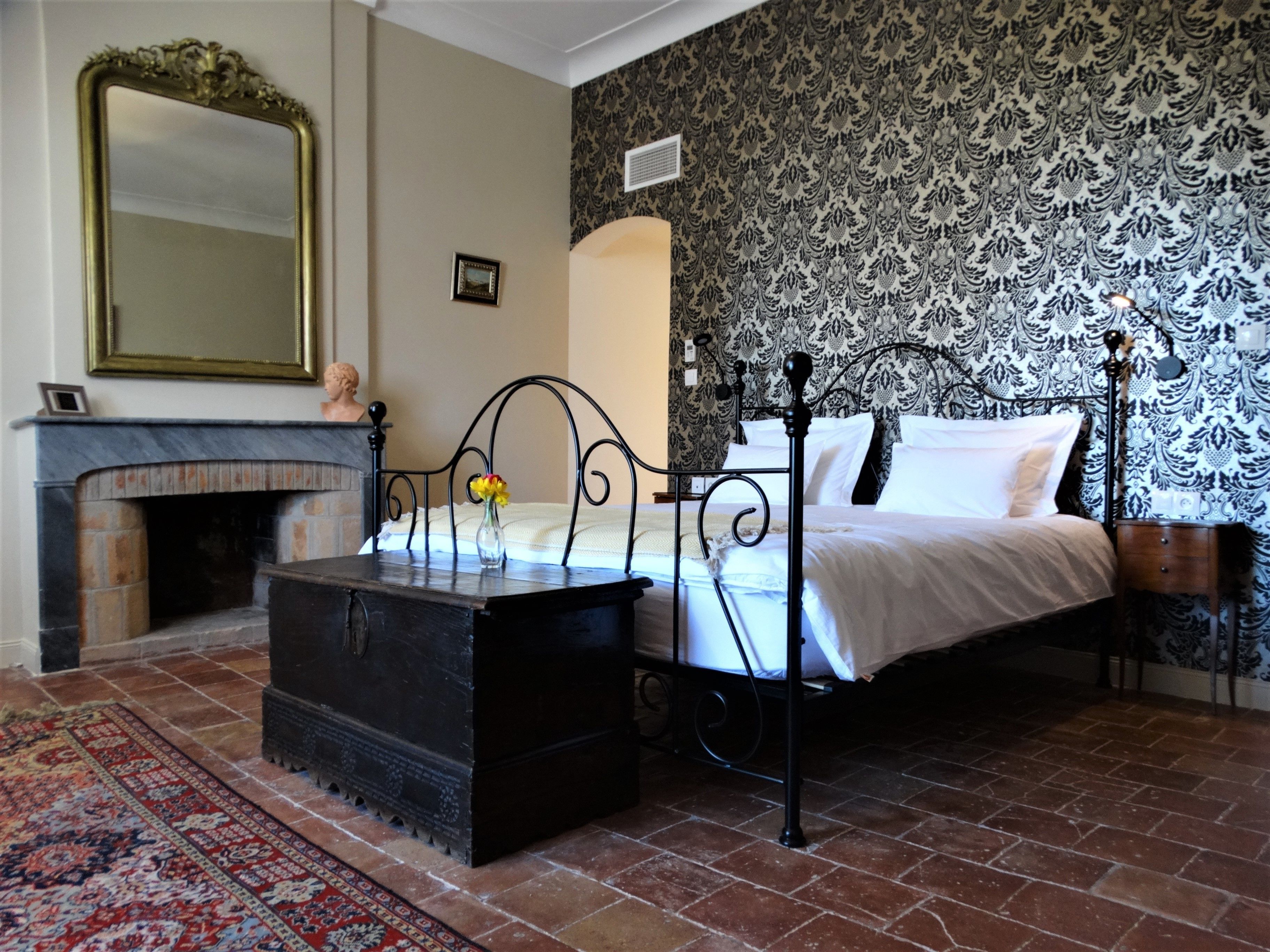 Un dormitorio con una cama con dosel, una chimenea, un espejo grande y papel tapiz estampado.
