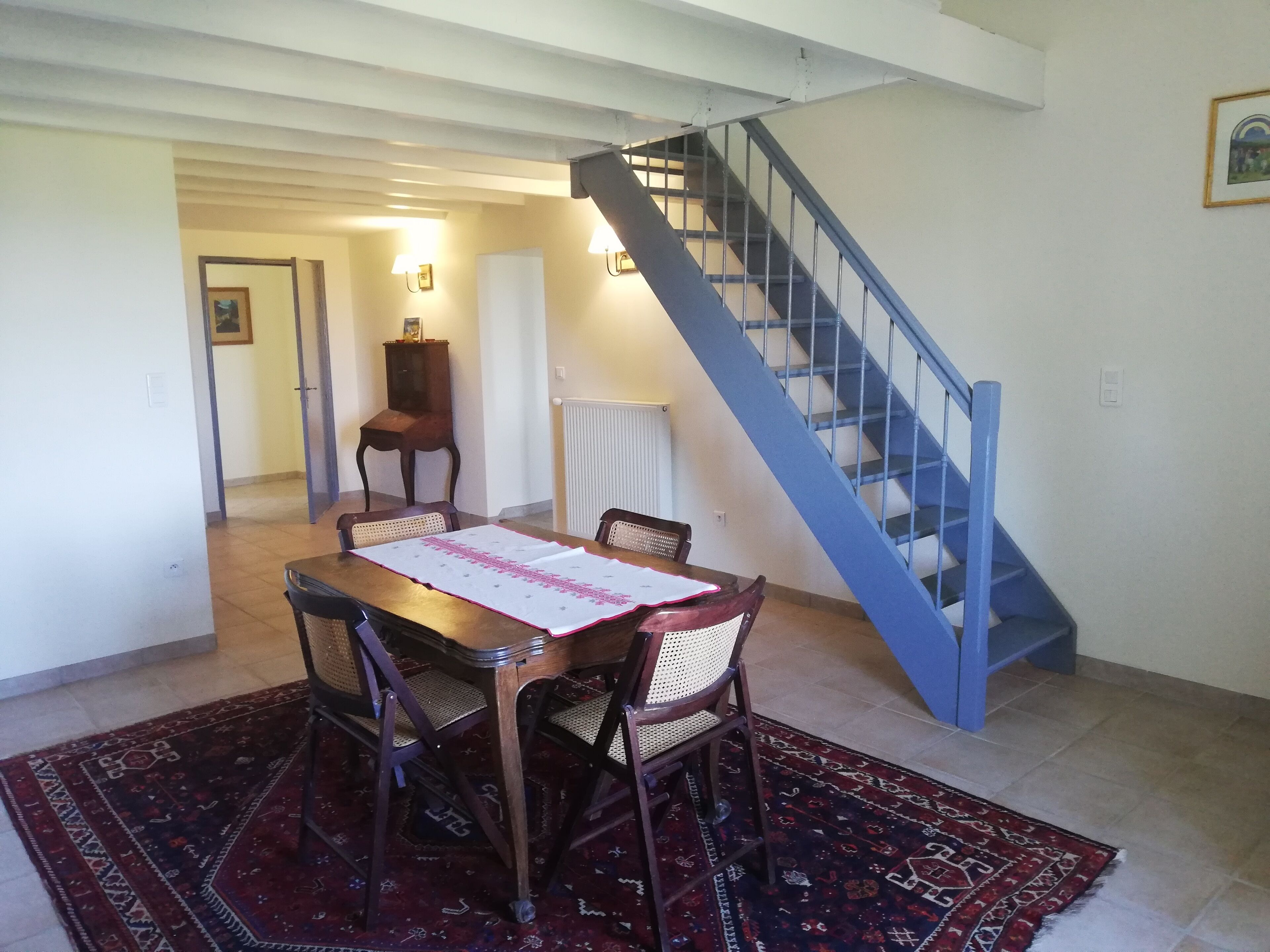 A dining area with a table set for four, a blue staircase, and a radiator.