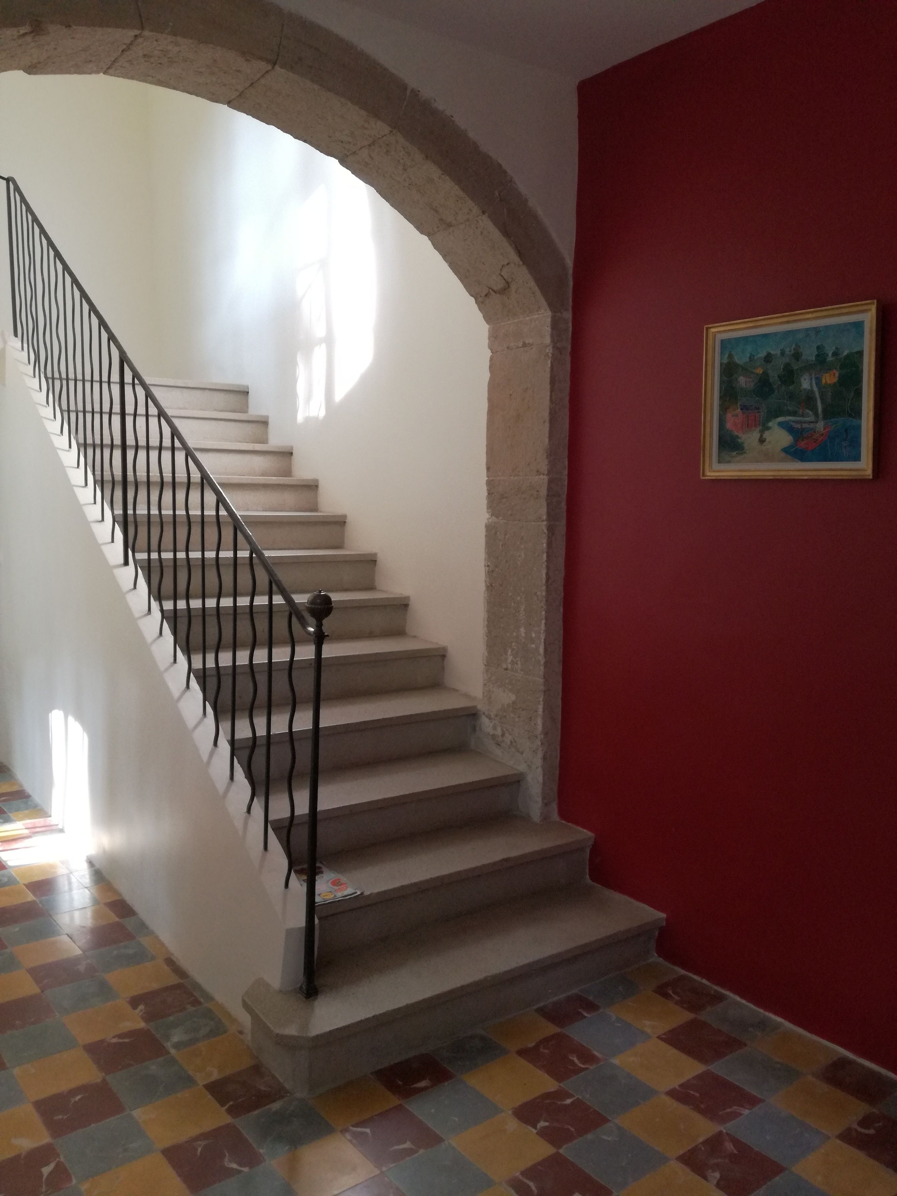 Eine Treppe mit Metallgeländer, eine rote Wand mit einem gerahmten Bild und ein Schachbrettfußboden.