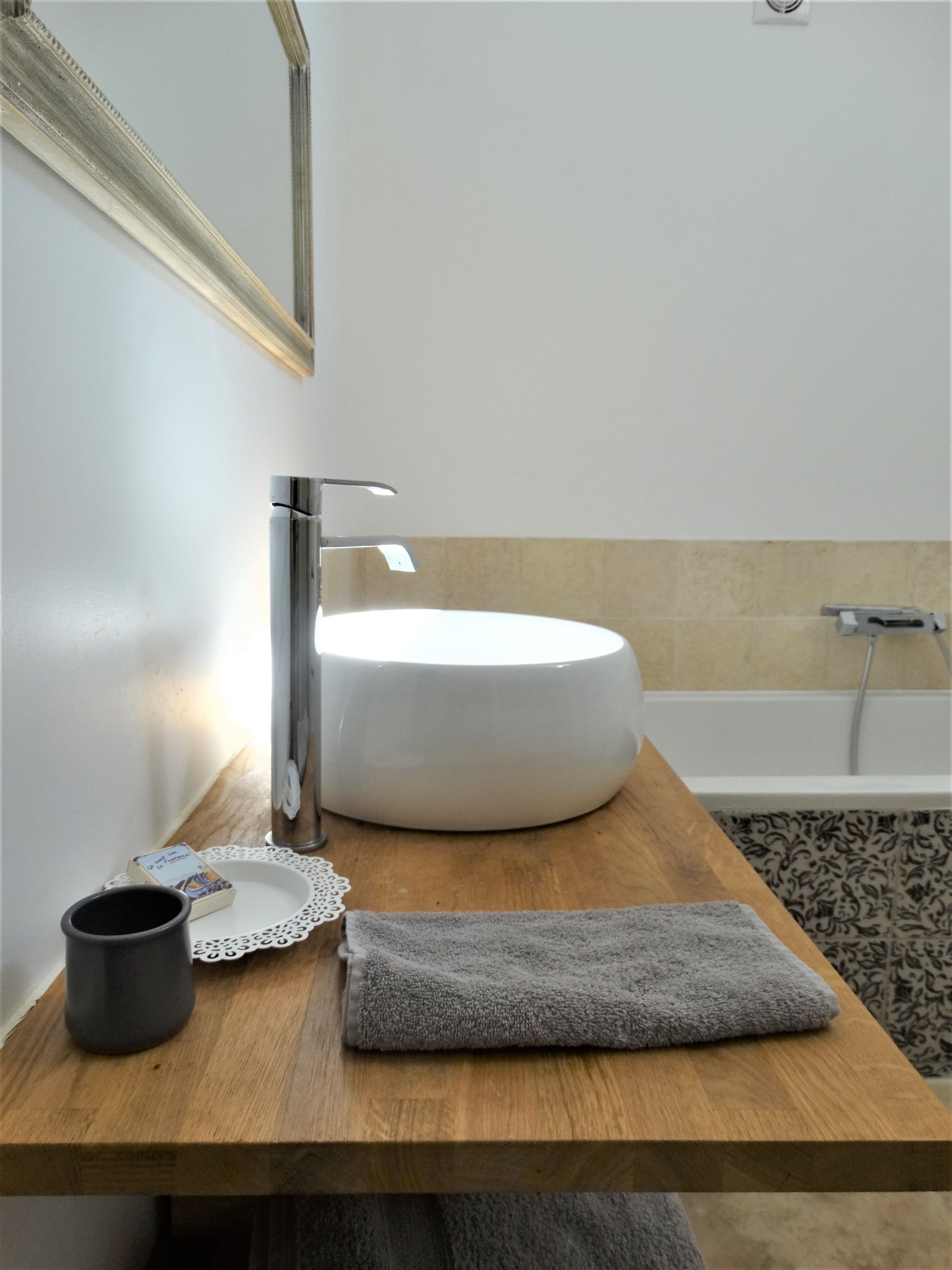 A bathroom with a round white sink, a mirror, a towel, and a bottle on a wooden countertop.