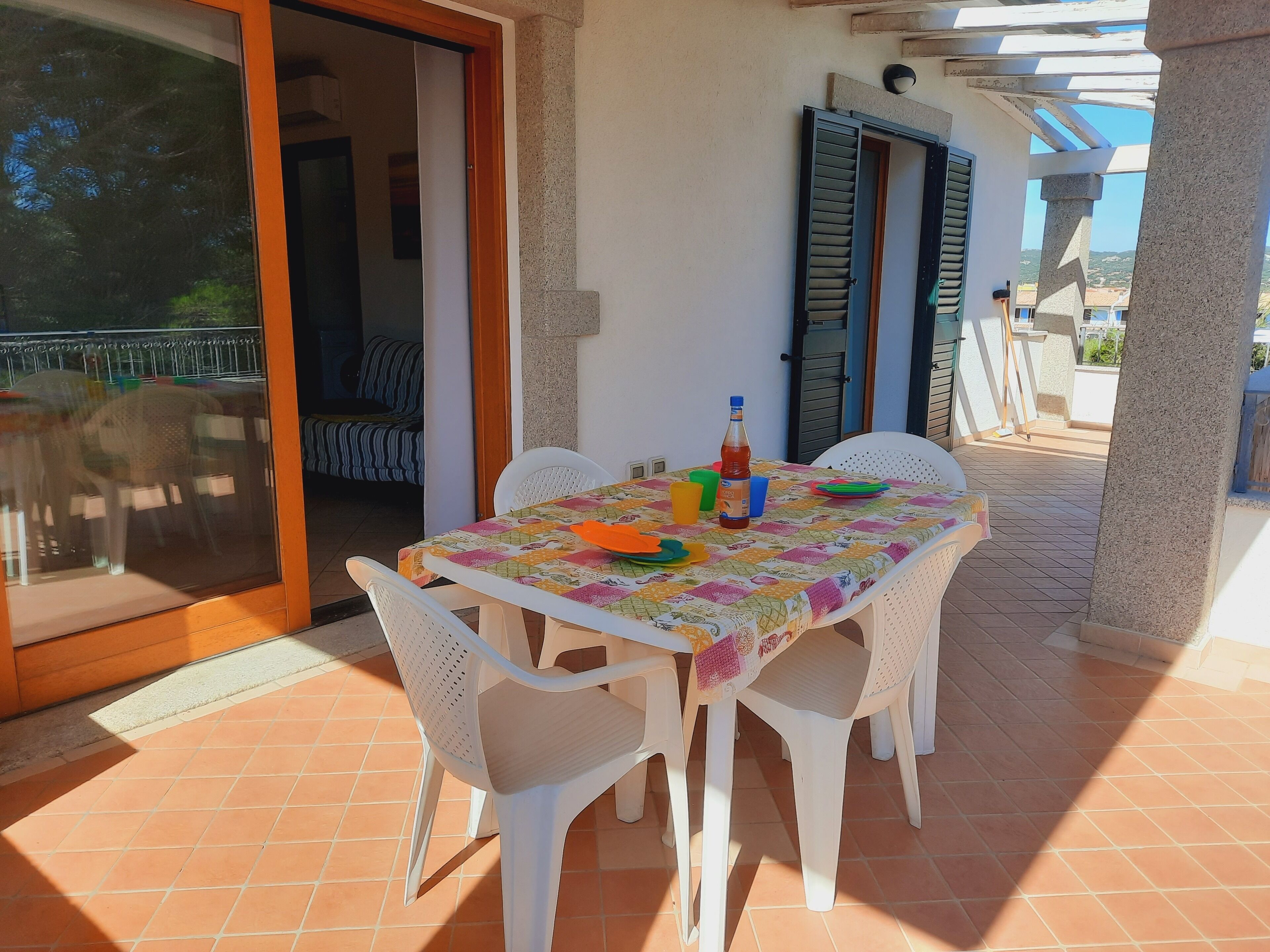 Un patio con una mesa dispuesta para cuatro personas, rodeado de sillas de plástico blanco.