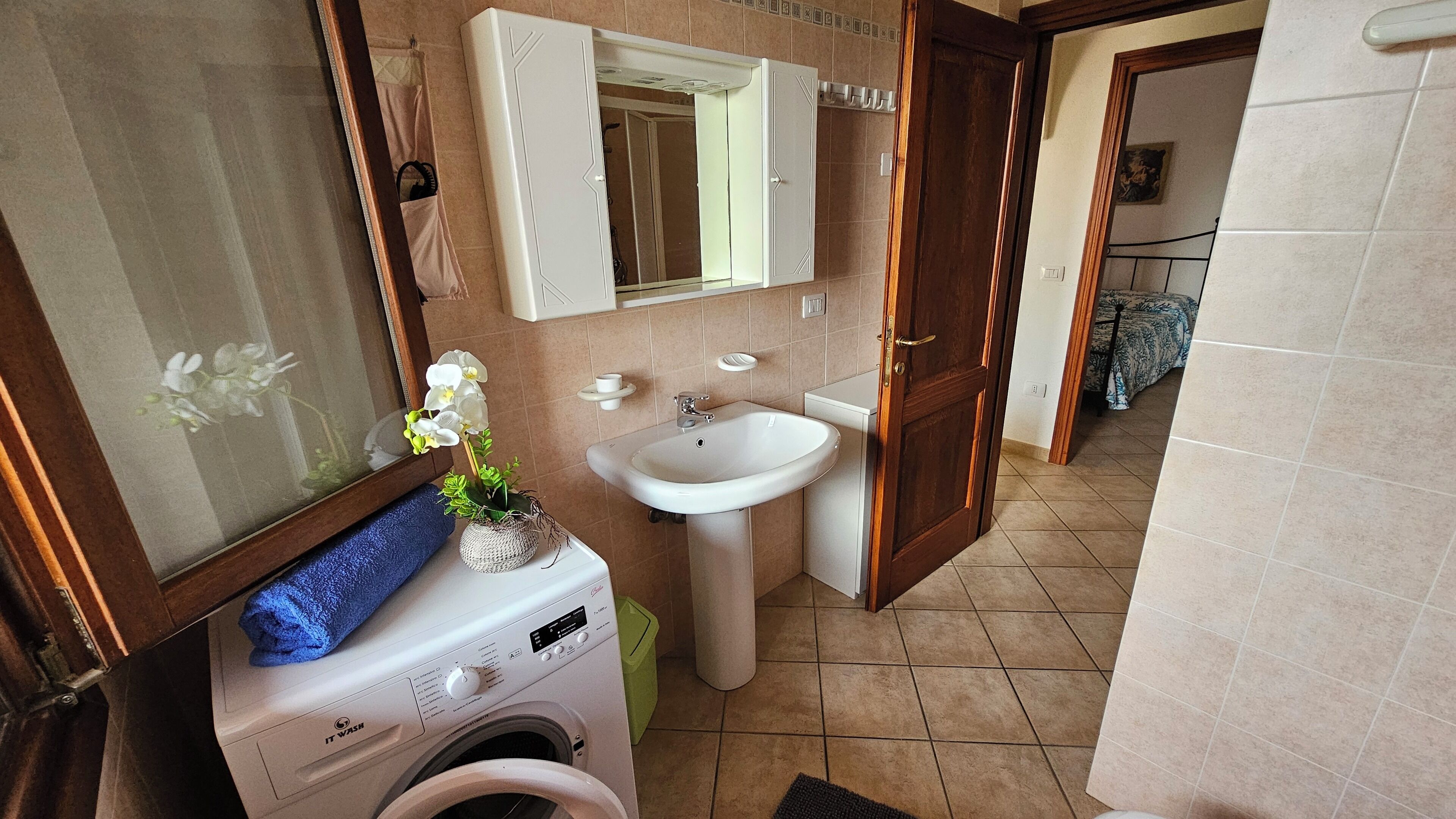 A compact bathroom with a washing machine, a sink, and a mirror.