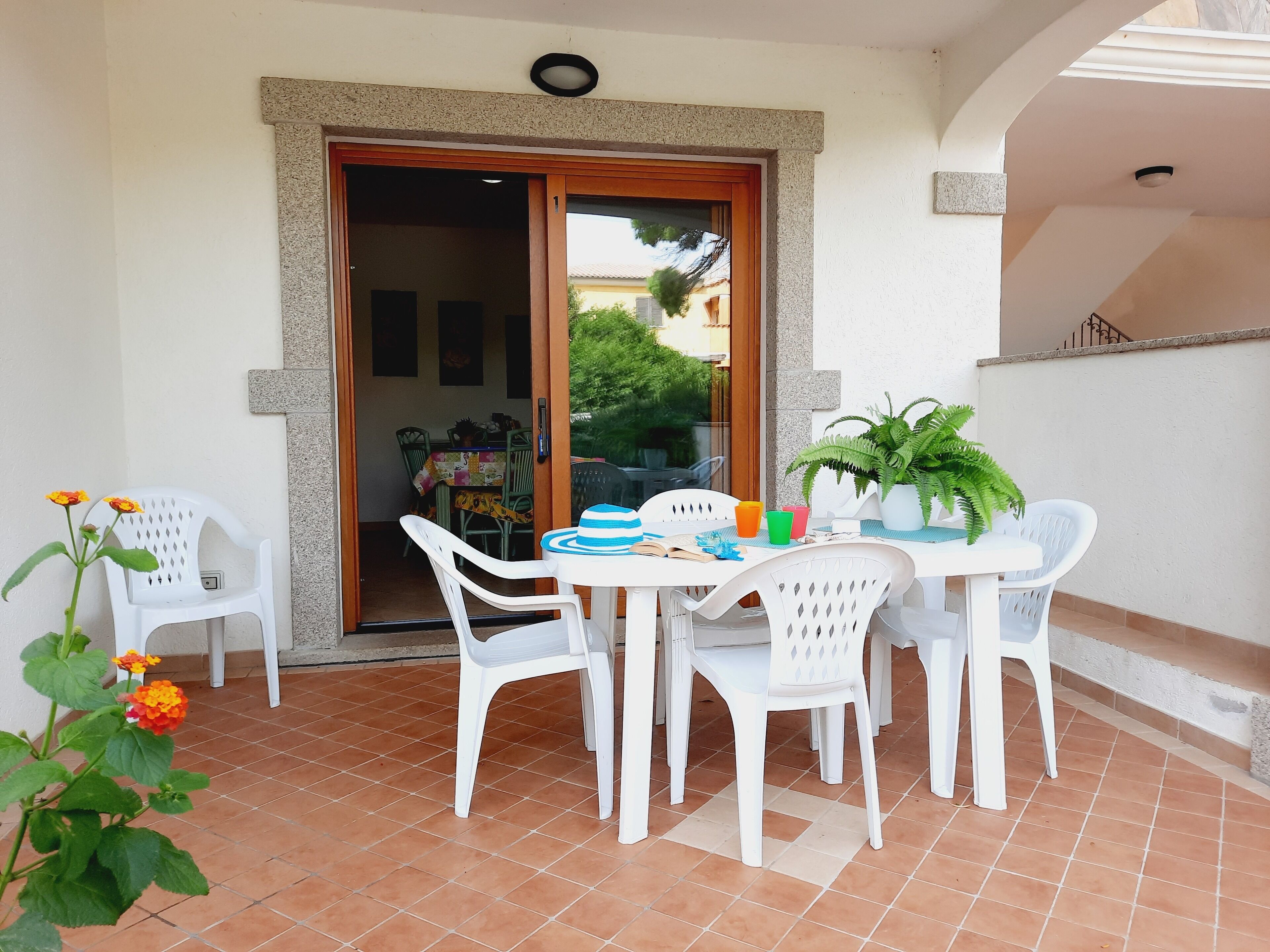 A patio with a table and chairs, a potted plant, and a door leading to an interior space.