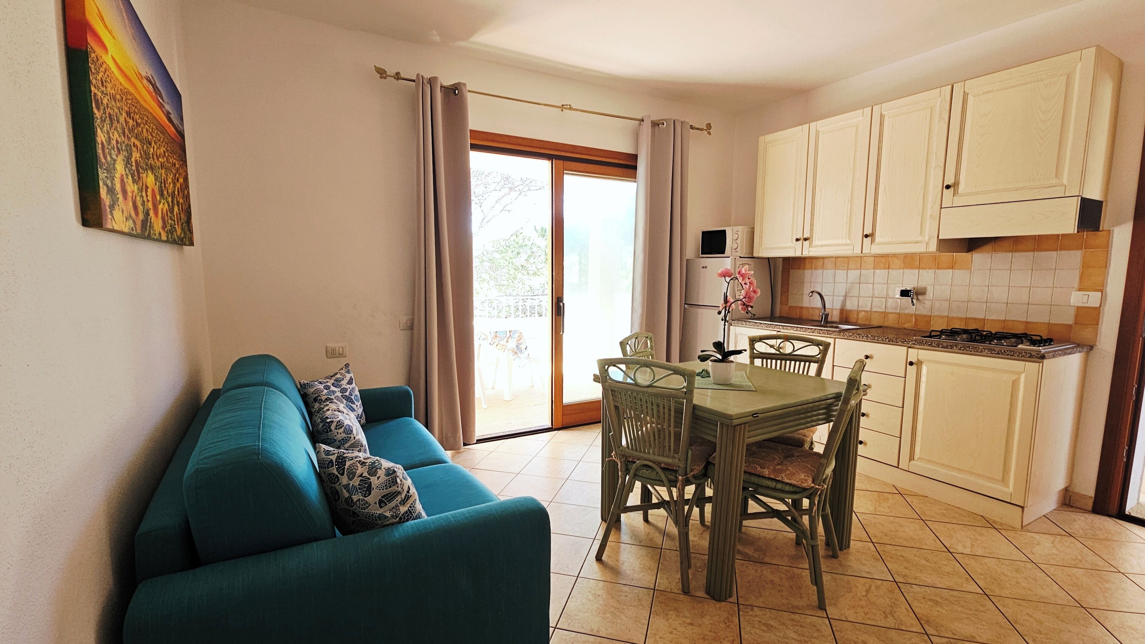A compact living space with a sofa, dining table, chairs, a kitchen area with cabinets, and a sliding glass door leading to an outdoor area.
