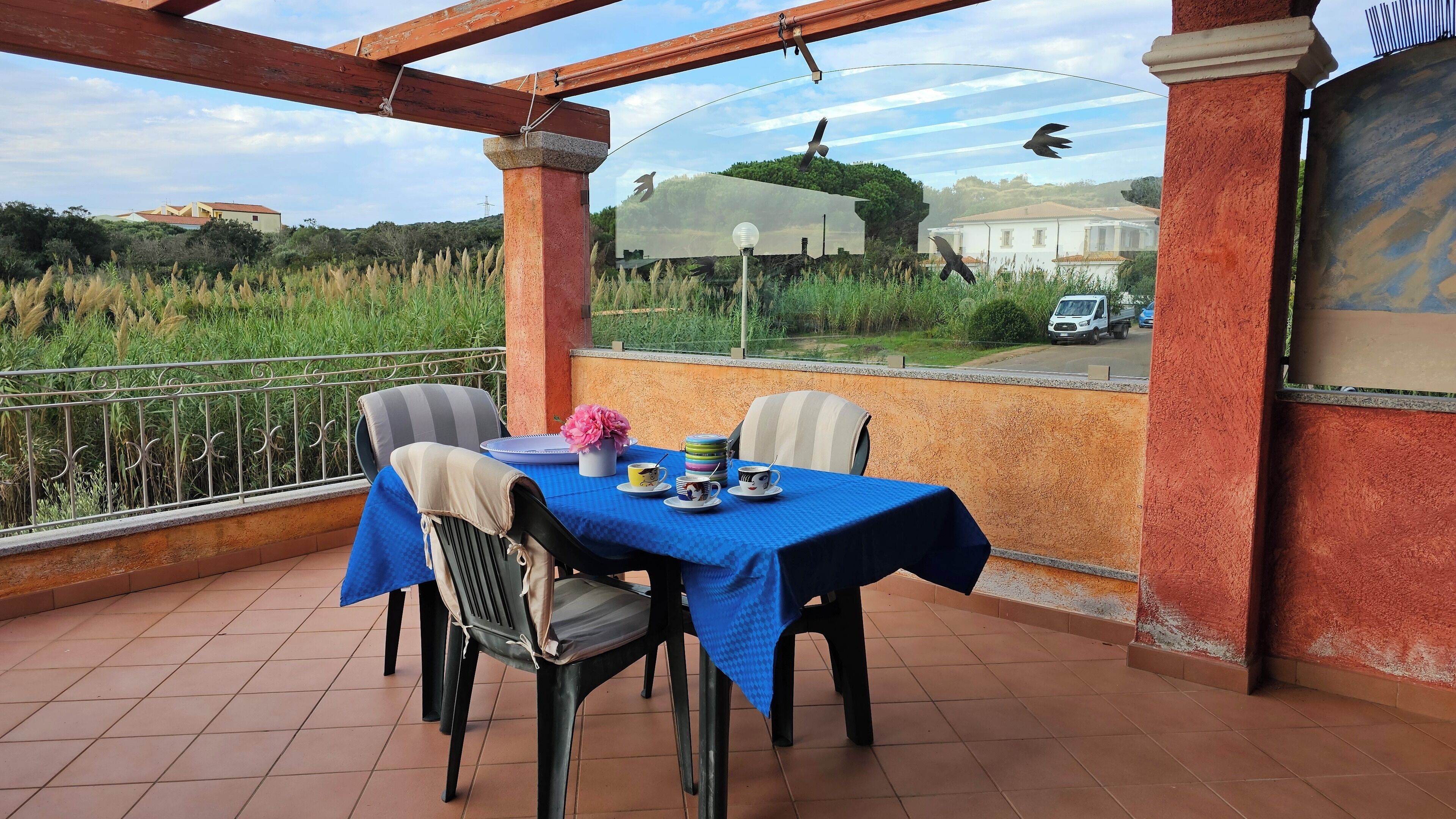 A balcony with a table set for two, chairs, and a view of a road with a vehicle.