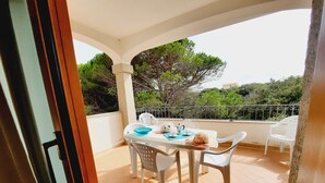 Un balcon avec une table dressée pour deux personnes, des chaises et une vue sur les arbres et les bâtiments.