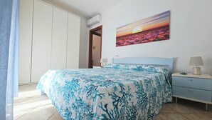 Une chambre à coucher avec un lit, une table de chevet, une lampe et un tableau représentant un coucher de soleil.