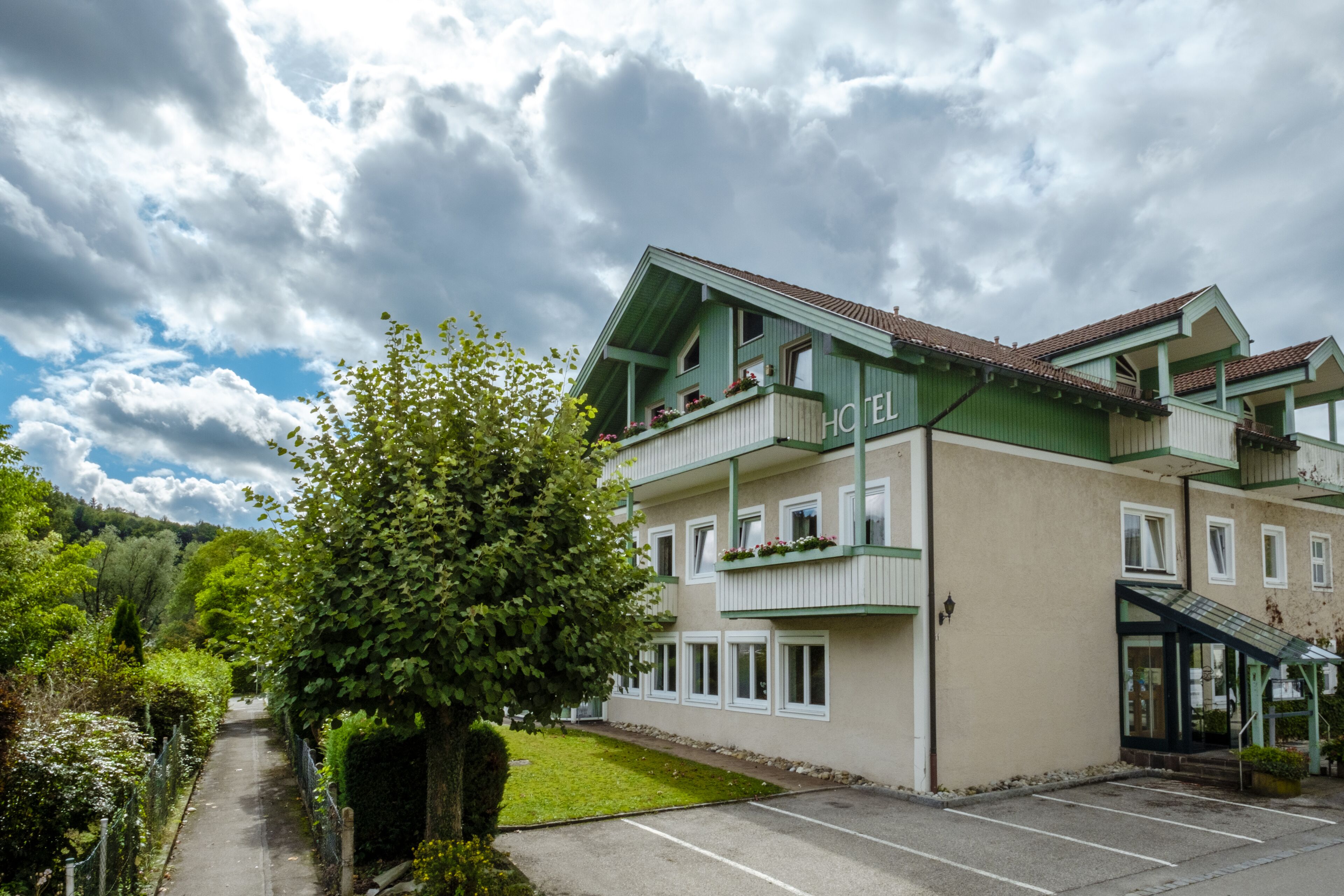 A hotel with a green facade, multiple balconies, and a parking area.