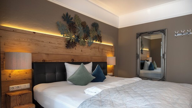 Een opgemaakt bed met een gewatteerde spreideken, twee bedlampen en een houten hoofdbord.
