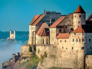 Un castillo histórico con múltiples torres y un edificio central destacado, situado sobre un acantilado con vistas a un valle.