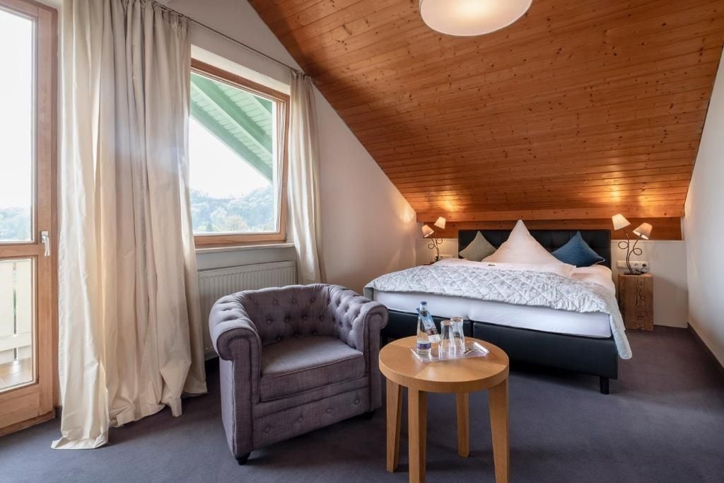 Un dormitorio con cama, una silla, una mesa y una ventana con cortinas.