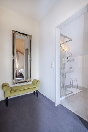 Relax in a serene space with a large mirror, plush bench, and modern bathroom featuring a glass shower enclosure.
