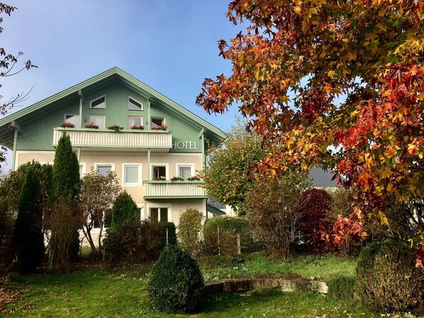Un hotel con fachada verde, varios balcones con jardineras y un jardín bien cuidado.