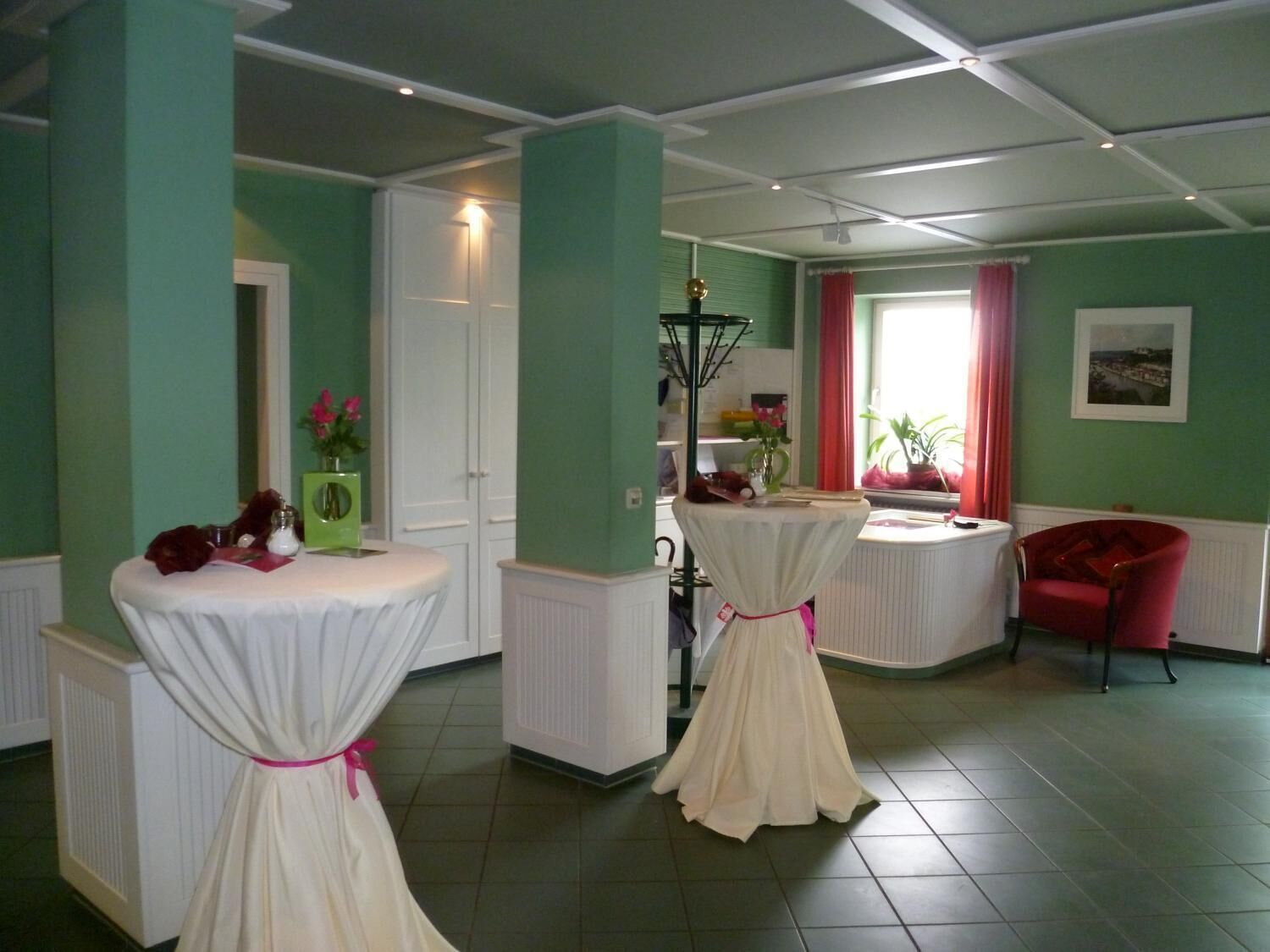 Una habitación con dos mesas blancas, una silla roja y una ventana con cortinas rojas.
