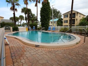 Una piscina de 3 pies con un patio de ladrillo, rodeada de palmeras y una valla blanca.