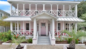 A two-story house with a porch, a pink door, and white railings.