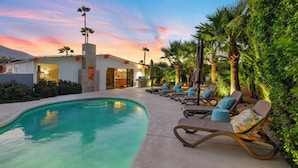 Un espace piscine avec des chaises longues, un bâtiment avec une entrée donnant accès à la piscine et un ciel au coucher du soleil.