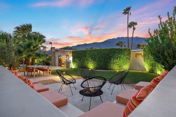 A modern outdoor patio with seating, a dining area, and a view of mountains at sunset.