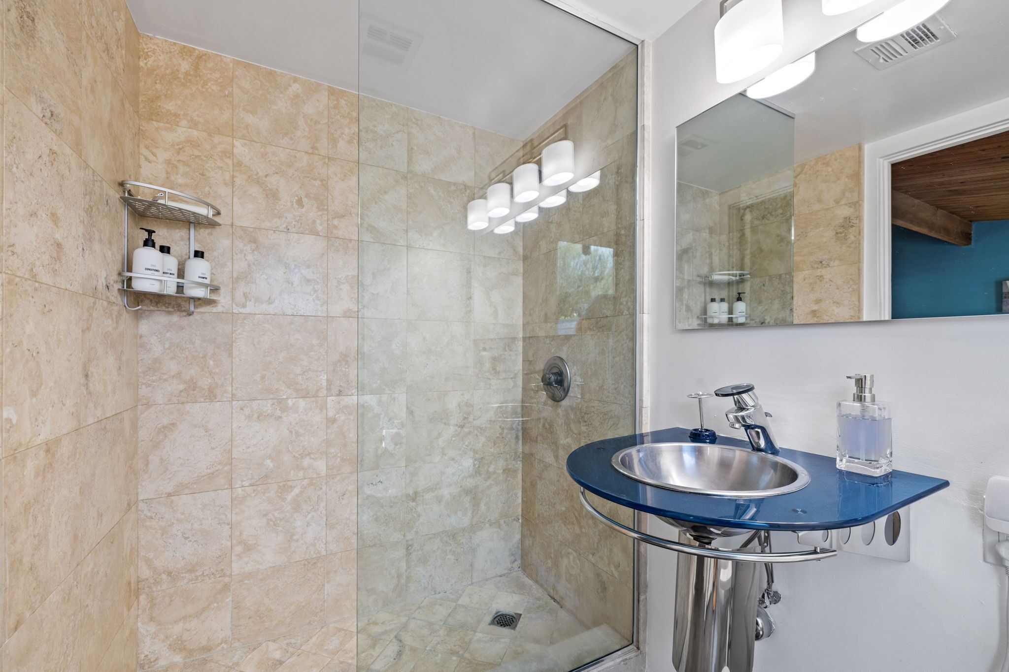A modern bathroom with a glass-enclosed shower, a blue sink, and a mirror.