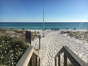 Une plage avec une promenade en bois menant au rivage, entourée de sable et d’une végétation clairsemée.