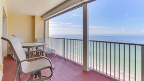 En balkon med et bord og stole, der vender ud mod en strand med gelænder.