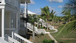 A white building with a balcony and a staircase leading to a lower level. - Condo w/Views, Beach, Htd Pool, Golf Cart, Kayaks, Gym, Pickleball Court! (Governors Harbour)