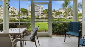 Un espacio exterior cubierto con una mesa y sillas, amplias ventanas que ofrecen vista a un puerto deportivo y edificios.