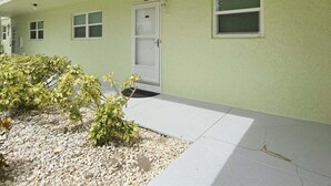 Un edificio de color verde claro, con puerta blanca y ventanas. Un pequeño jardín con plantas y guijarros en la parte delantera.