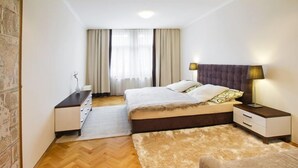 Ein Schlafzimmer mit Bett, Nachttischen, einem Schminktisch, einem Teppich und einem Fenster mit Vorhängen.