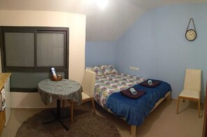 Ein kleines, gemütliches Zimmer mit einem Einzelbett, einem kleinen Tisch, einem Stuhl und einer Wanduhr.