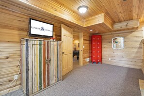 A wooden interior with a television displaying "RENTBRIINS.COM", a red storage unit, and a red cabinet with drawers. - Elegant 2700 Sq Ft True Log Cabin-Private Hot Tub-Game Room-Pool Table-Best View Near Big Cedar (Ridgedale)