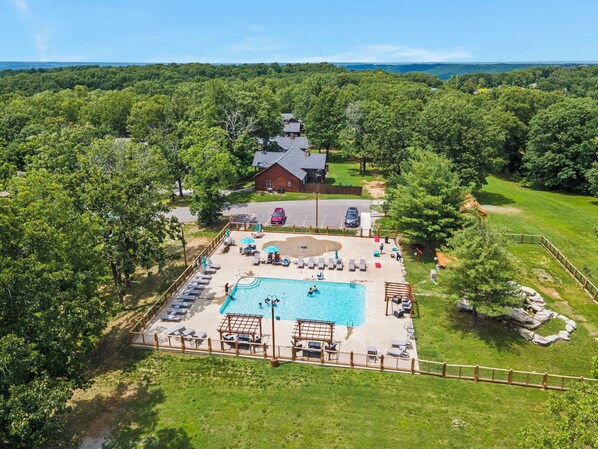 An aerial view of a resort with a swimming pool, lounge chairs, and a rustic building. - Elegant 2700 Sq Ft True Log Cabin-Private Hot Tub-Game Room-Pool Table-Best View Near Big Cedar (Ridgedale)