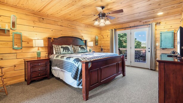 A wooden-paneled bedroom with a bed, nightstands, a dresser, and a ceiling fan. - Elegant 2700 Sq Ft True Log Cabin-Private Hot Tub-Game Room-Pool Table-Best View Near Big Cedar (Ridgedale)