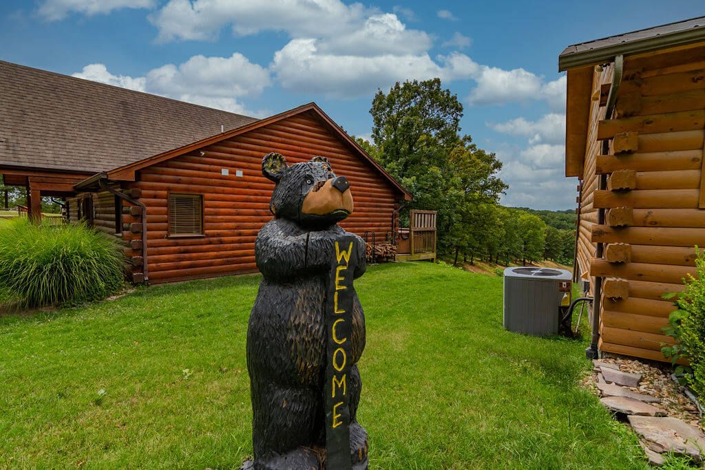 A wooden cabin with a bear statue in the yard.