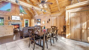 A spacious wooden cabin interior with a dining area, fireplace, and large wooden doors.