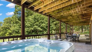 A hot tub under a wooden pergola with a view of trees.