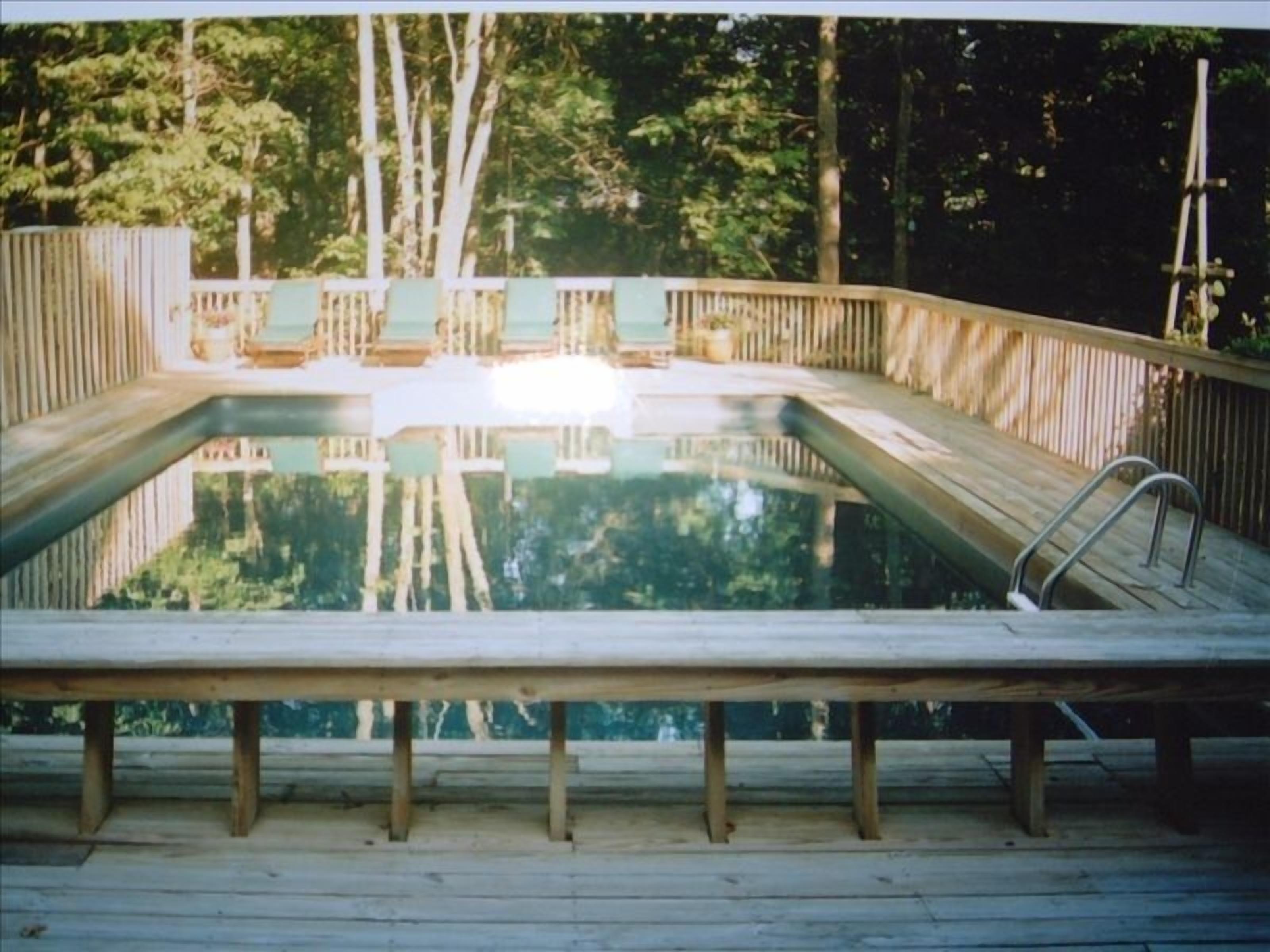 A wooden deck with a swimming pool, surrounded by trees.