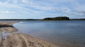 En sandstrand med stilla vatten och en skogbeklädd ö i fjärran.