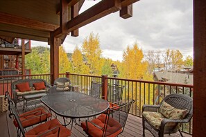 Überdachte Terrasse im Freien mit einem runden Tisch und Korbstühlen, mit Blick auf eine Wohngegend im Herbstlaub.