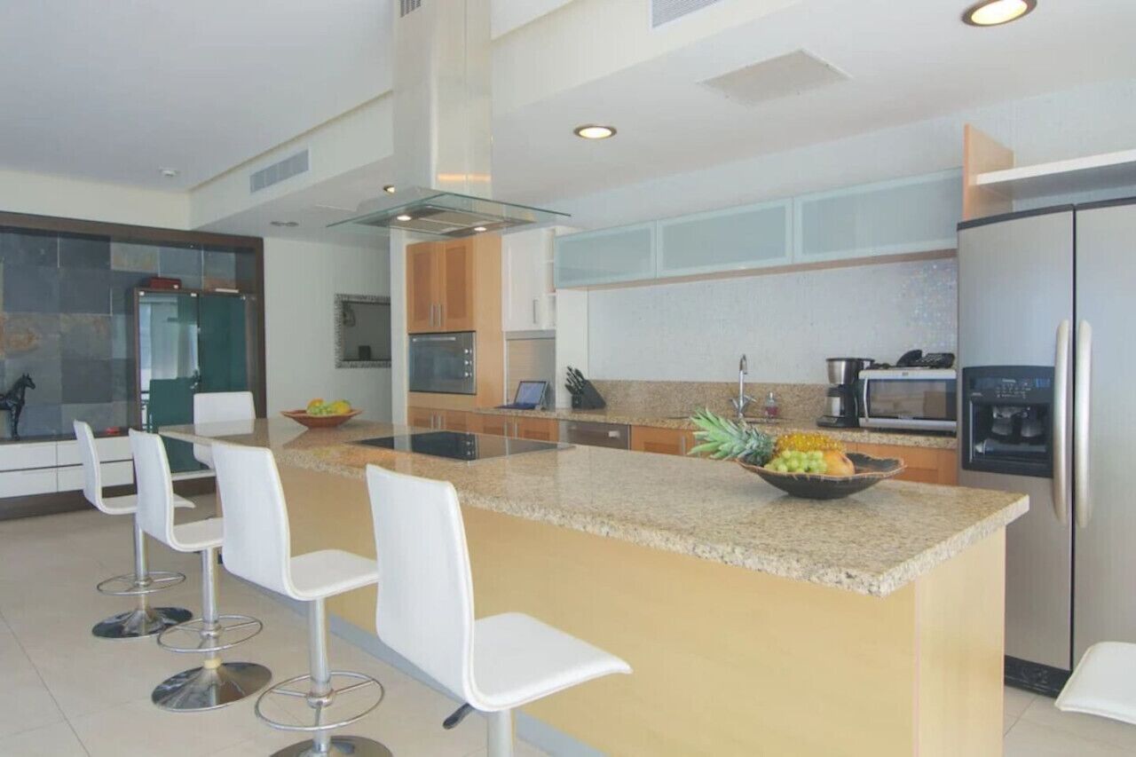 Una cocina moderna con una isla central, taburetes de bar y un refrigerador.