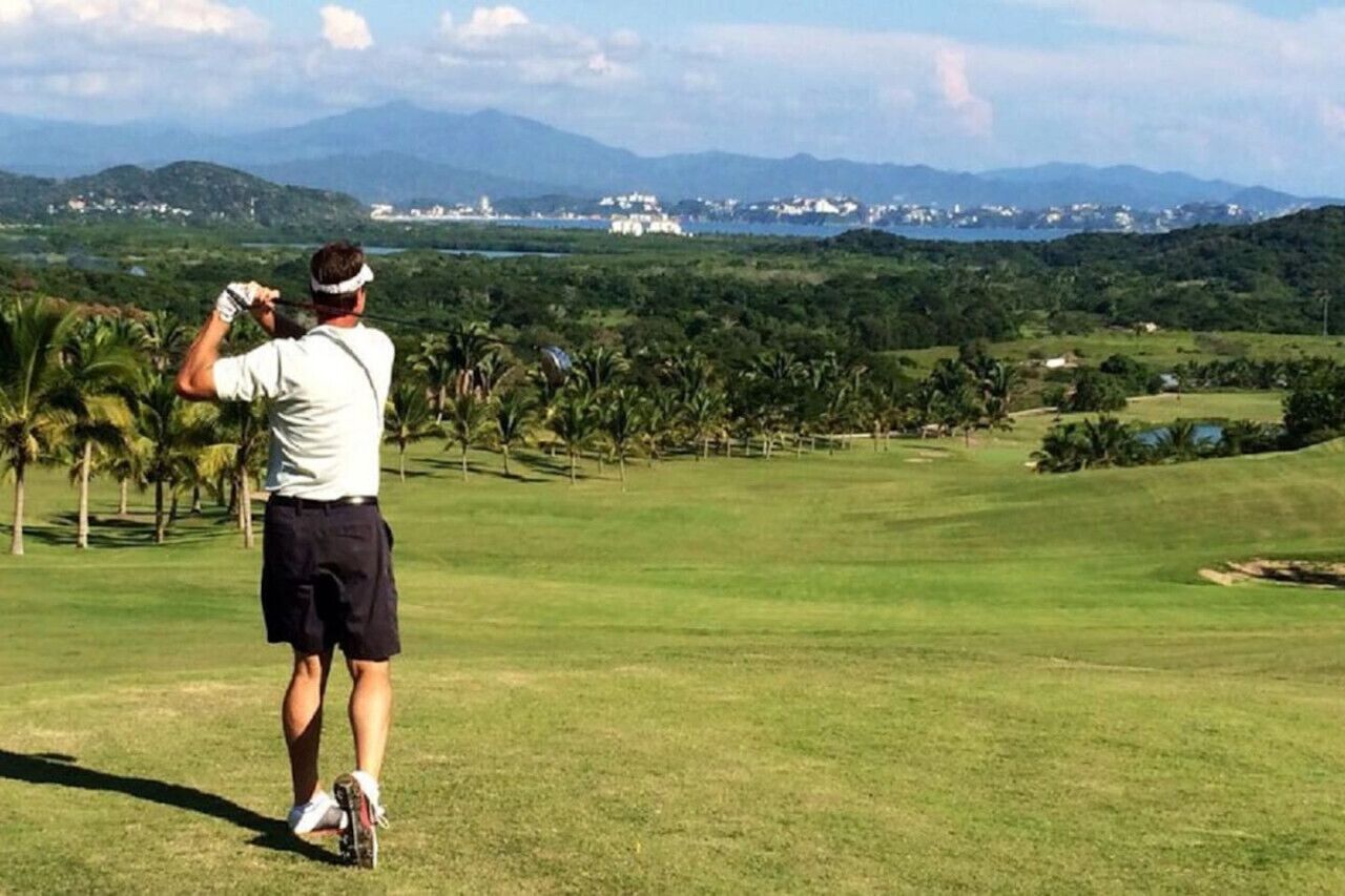 Ein Golfplatz mit einer Person in weißem Hemd und schwarzen Shorts, die bereit ist, einen Golfschläger zu schwingen.