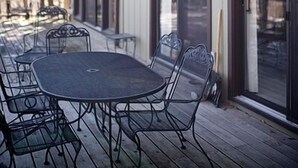 Un patio cubierto con una mesa redonda y sillas, puertas correderas de vidrio y una terraza de madera.