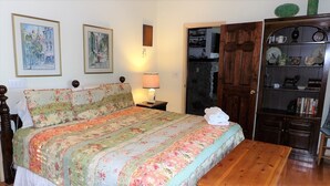 Un dormitorio con una colcha de flores, una lámpara de noche, un armario de madera y dos cuadros en la pared.
