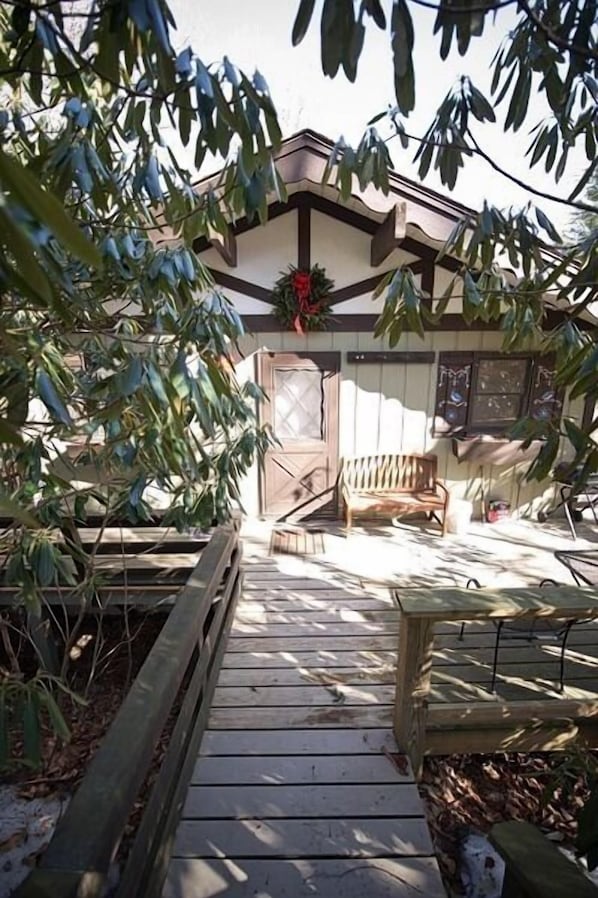 Une terrasse en bois mène à un bâtiment doté d’un toit brun et d’une guirlande rouge.