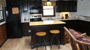 Una cocina con armarios de madera oscura, un refrigerador negro, un microondas, una estufa, dos taburetes y una barra de bar de madera.