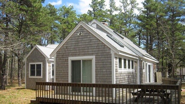 A two-story cabin with a deck and a large sliding door. - Newly Updated Spacious Home in Quiet Wooded Area (1246) (Wellfleet)