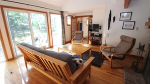 A wooden-floored living room with a sofa, two chairs, a coffee table, and a fireplace. - Newly Updated Spacious Home in Quiet Wooded Area (1246) (Wellfleet)