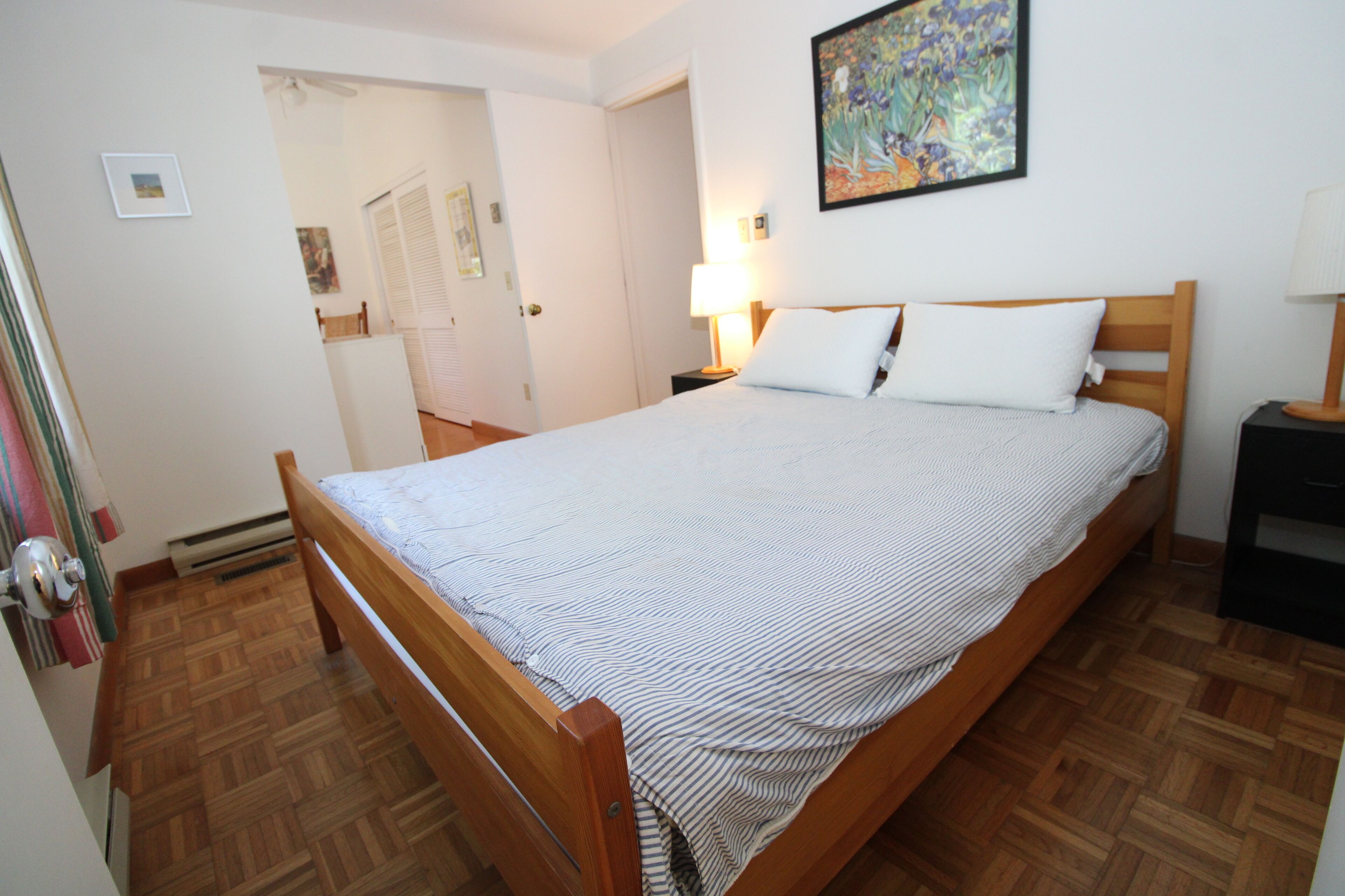 Un dormitorio con una cama de madera, una mesita de noche, una lámpara y un cuadro en la pared.