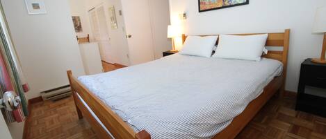Un dormitorio con una cama de madera, una mesita de noche, una lámpara y un cuadro en la pared.