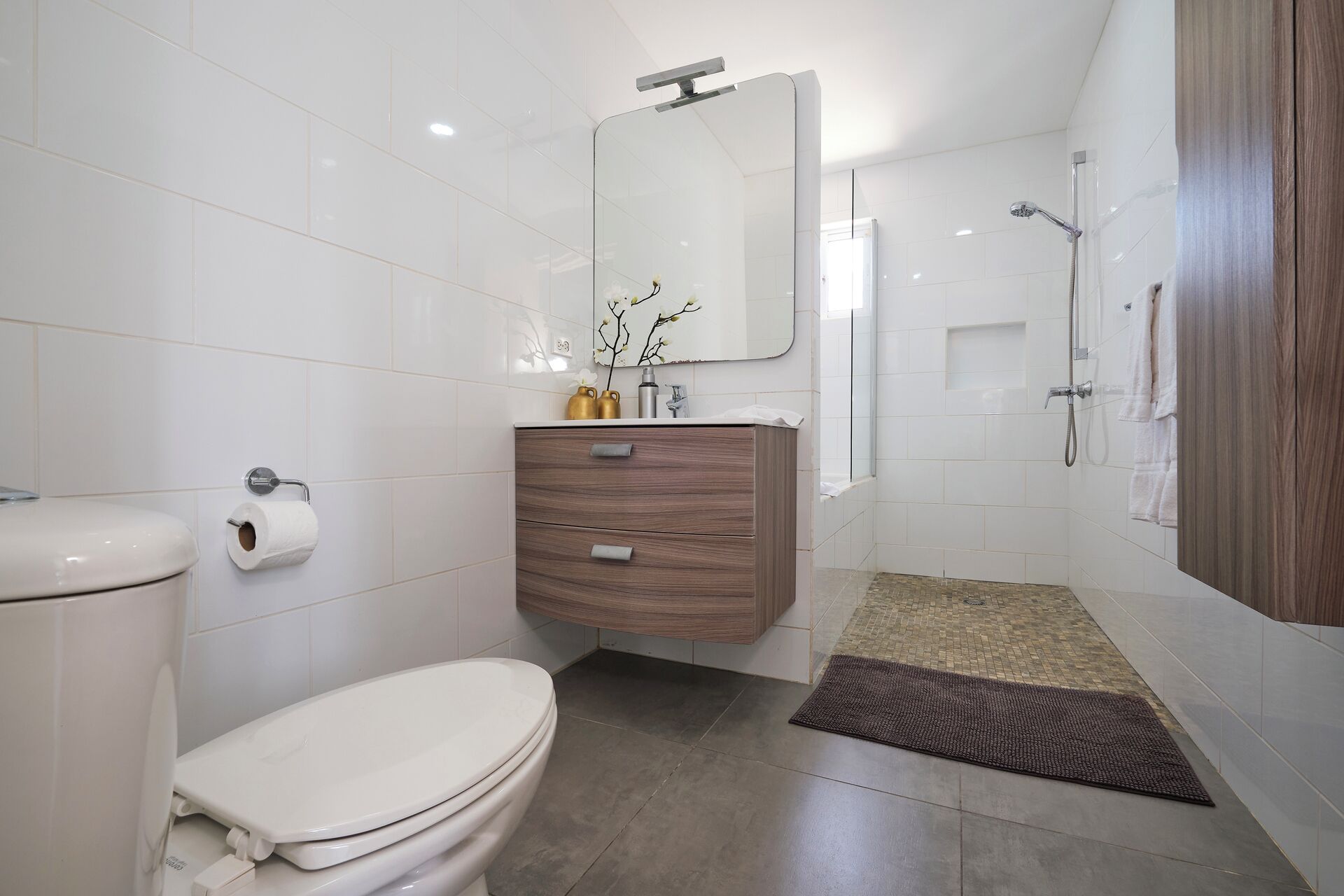 A modern bathroom with a toilet, vanity, mirror, shower, and a small rug.